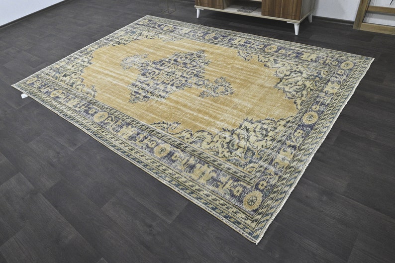 May include: A vintage-style rug with a beige background and a blue and white floral pattern. The rug has a distressed look and a fringed edge.