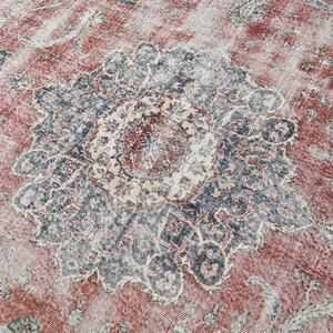 Pode incluir: Um tapete vintage com fundo vermelho desbotado e um grande padr&atilde;o floral azul e branco intrincado no centro.