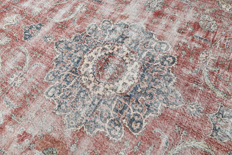 Pode incluir: Um tapete vintage com fundo vermelho desbotado e um grande padr&atilde;o floral azul e branco intrincado no centro.