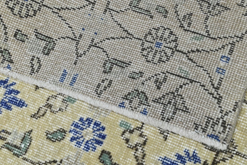 May include: Close-up of a beige and cream patterned rug with blue and green accents. The rug has a fringe border.