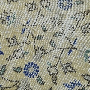 May include: A close-up of a beige rug with a floral pattern. The rug has a subtle sheen and features blue, green, and brown accents.