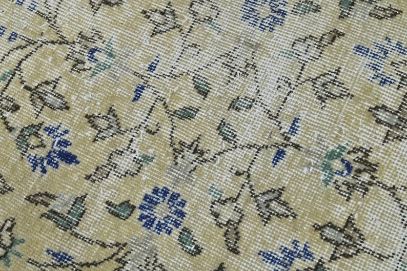 May include: A close-up of a beige rug with a floral pattern. The rug has a subtle sheen and features blue, green, and brown accents.
