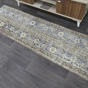 May include: A long, rectangular runner rug with a beige background and a blue and cream floral pattern. The rug has a distressed, vintage look.