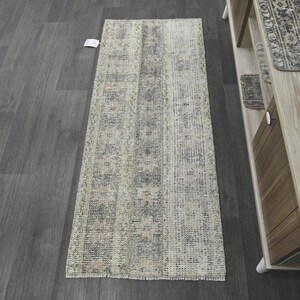 May include: A long, rectangular runner rug with a distressed, vintage-inspired pattern in shades of beige, gray, and blue. The rug has a fringed edge.