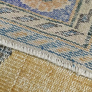 May include: Close-up of a woven rug with a fringe border. The rug has a geometric pattern in shades of blue, brown, and beige.