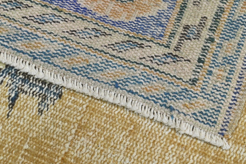 May include: Close-up of a woven rug with a fringe border. The rug has a geometric pattern in shades of blue, brown, and beige.