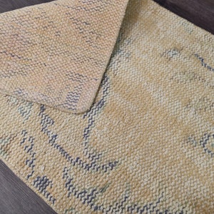 K&ouml;nnte beinhalten: Ein beiger Teppich mit einem gewebten Muster aus blauen Linien. Der Teppich ist in der Mitte gefaltet und hat eine strukturierte Oberfl&auml;che.
