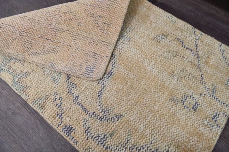 K&ouml;nnte beinhalten: Ein beiger Teppich mit einem gewebten Muster aus blauen Linien. Der Teppich ist in der Mitte gefaltet und hat eine strukturierte Oberfl&auml;che.