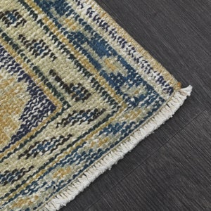 May include: Close-up of a woven rug with a fringe edge. The rug has a geometric pattern in shades of blue, yellow, and white.