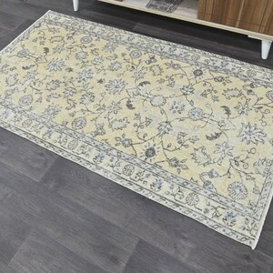 May include: A light beige rug with a floral pattern in shades of gray and blue. The rug has a border with a repeating pattern.