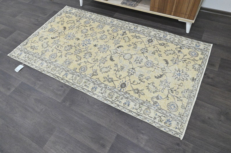 May include: A light beige rug with a floral pattern in shades of gray and blue. The rug has a border with a repeating pattern.