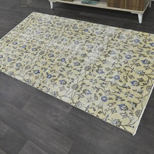 May include: A cream-colored rug with a floral pattern in shades of blue and gray. The rug has a distressed look, giving it a vintage feel.