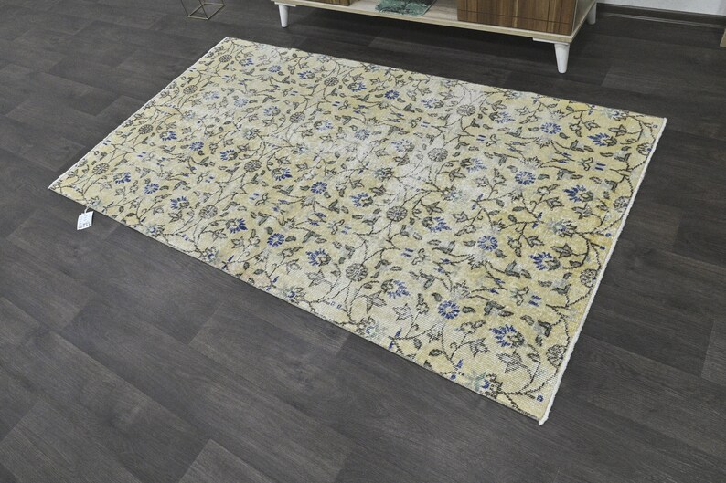 May include: A cream-colored rug with a floral pattern in shades of blue and gray. The rug has a distressed look, giving it a vintage feel.