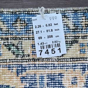 Op de afbeelding: Een wit label met zwarte tekst met de afmetingen van een tapijt in voet, inch en centimeter. Het label geeft ook de oppervlakte van het tapijt in vierkante meter en het gewicht in kilogram weer. Het label heeft een barcode en het nummer 7451 staat erop gedrukt.