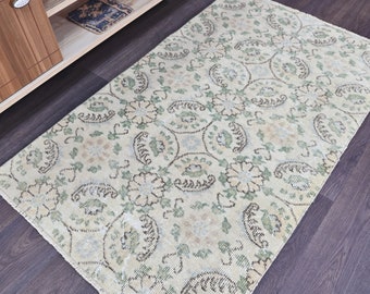 May include: A cream-colored rug with a green and brown floral pattern. The rug has a distressed look and is made of a soft, woven material.