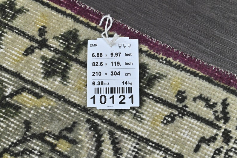May include: A white tag with black text and a barcode. The tag lists the dimensions of a rug in feet, inches, and centimeters. The rug is 6.88 feet by 9.97 feet, 82.6 inches by 119 inches, and 210 centimeters by 304 centimeters. The tag also lists the rug's area as 6.38 square meters and its weight as 14 kilograms. The tag number is 10121.