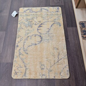 K&ouml;nnte beinhalten: Ein hellgelber und blauer Teppich mit einem floralen Muster. Der Teppich ist aus einem weichen, gewebten Material gefertigt und hat einen Fransenrand.