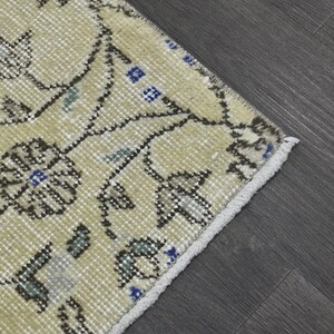 May include: A cream-colored rug with a floral pattern in shades of brown, blue, and green. The rug has a fringe border.