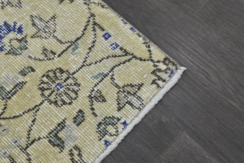 May include: A cream-colored rug with a floral pattern in shades of brown, blue, and green. The rug has a fringe border.