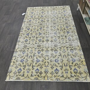 May include: A vintage-style rug with a cream background and a floral pattern in shades of blue and gray. The rug has a distressed look, with faded colors and a worn texture.
