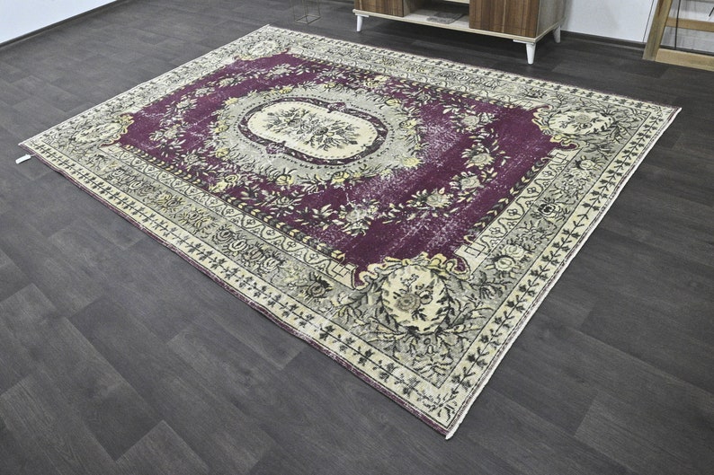 May include: A vintage rug with a floral pattern in shades of purple, cream, and black. The rug has a distressed look and a fringed edge.