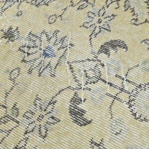 May include: Close-up of a cream-colored rug with a floral pattern in shades of gray and blue. The rug has a woven texture and shows signs of wear.