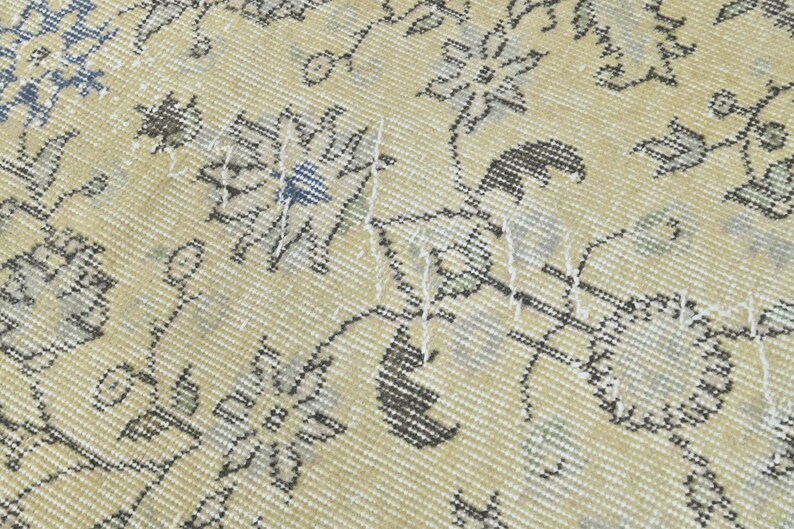 May include: Close-up of a cream-colored rug with a floral pattern in shades of gray and blue. The rug has a woven texture and shows signs of wear.