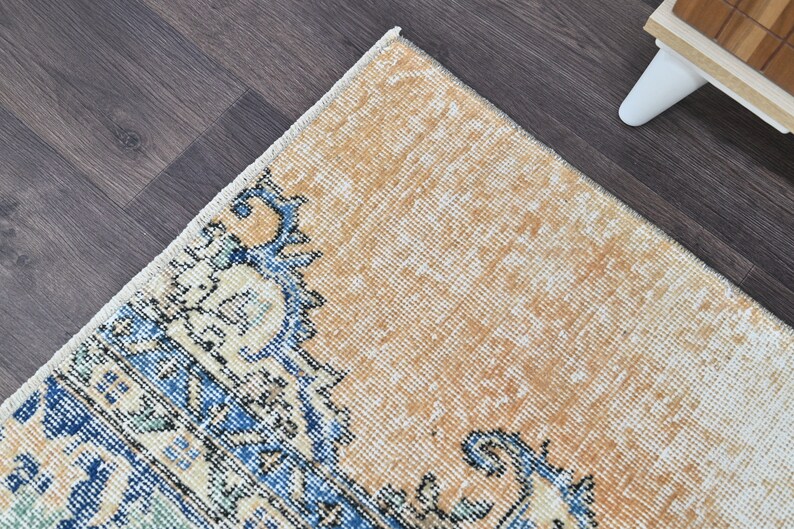 Op de afbeelding: Een vintage tapijt met een verbleekte oranje achtergrond en een blauw en wit bloemenpatroon. Het tapijt heeft een verweerde uitstraling en is gemaakt van een zacht, geweven materiaal.