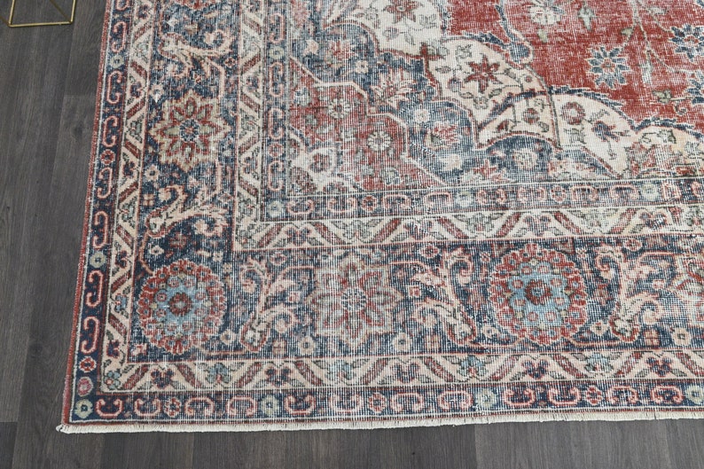 Pode incluir: Um tapete vintage com um padr&atilde;o floral desbotado em vermelho, azul e branco. O tapete tem um aspecto desgastado e uma borda franjada.