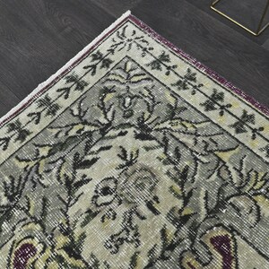 May include: A vintage rug with a floral pattern in shades of gray, black, and white. The rug has a burgundy border with a white fringe.
