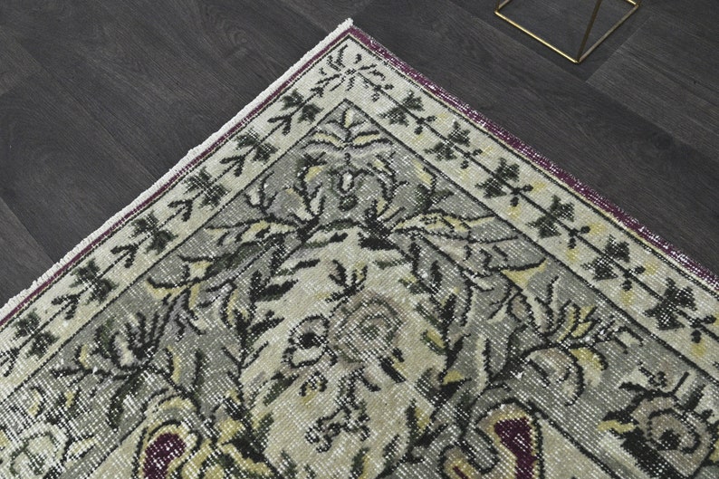 May include: A vintage rug with a floral pattern in shades of gray, black, and white. The rug has a burgundy border with a white fringe.