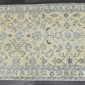 May include: A vintage rug with a cream background and a floral pattern in shades of blue and brown. The rug has a border with a repeating pattern of circles and flowers.