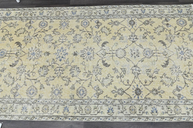 May include: A vintage rug with a cream background and a floral pattern in shades of blue and brown. The rug has a border with a repeating pattern of circles and flowers.