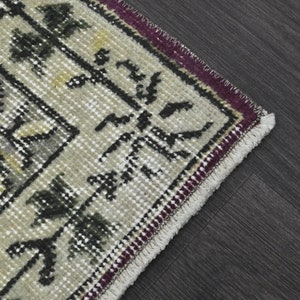 May include: Close-up of the edge of a beige rug with a black and white geometric pattern. The rug has a burgundy and white fringe.