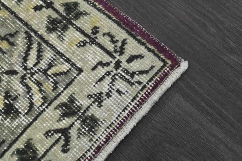 May include: Close-up of the edge of a beige rug with a black and white geometric pattern. The rug has a burgundy and white fringe.