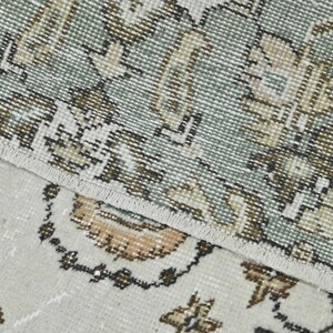 Op de afbeelding: Close-up van een tapijt met een gedetailleerd bloemenpatroon in beige, bruin en groene tinten. Het tapijt heeft een witte franje rand.