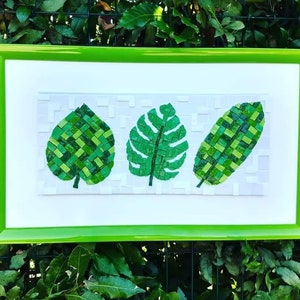 Peut inclure: Une œuvre d'art en mosaïque encadrée représentant trois feuilles vertes. Les feuilles sont faites de petites tuiles vertes et sont disposées selon un motif symétrique. Le cadre est vert vif.