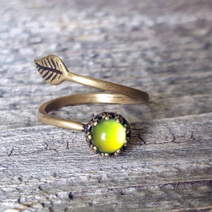 May include: A gold-toned ring with a green iridescent stone and a leaf design. The ring is adjustable and can be worn on any finger.