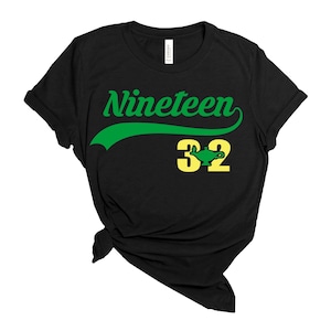 以下が含まれることがあります： 「Nineteen 32」と緑色のランプのグラフィックが書かれた、緑と黄色のグラフィックが施された黒いTシャツです。