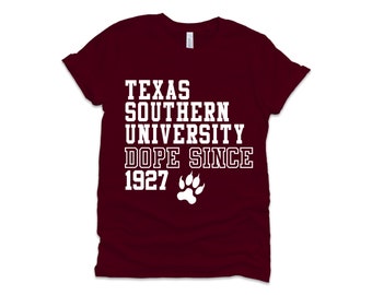 Op de afbeelding: Een maroon t-shirt met witte tekst die "Texas Southern University Dope Since 1927" zegt en een witte pootafdruk.