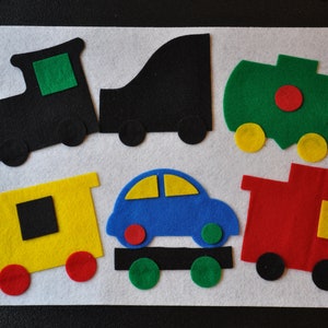 Peut inclure: Un ensemble de jeu en feutre avec une locomotive noire, un wagon jaune, un wagon-citerne vert, un wagon rouge, une voiture bleue et un camion noir. L'ensemble est sur un fond blanc.
