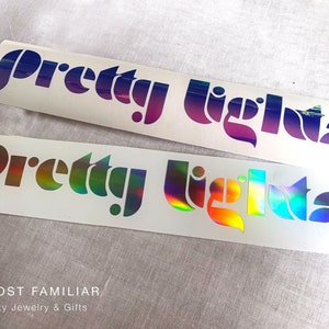 May include: Two white stickers with the text "Pretty Lights" in a rainbow iridescent font. The top sticker has a purple and blue gradient, while the bottom sticker has a rainbow gradient.