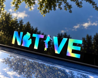 May include: A holographic decal applied to a vehicle window displaying the word NATIVE in bold capital letters. The letter A is replaced by the outline of the state of Michigan, and the letter I is replaced by a vertical map shape.