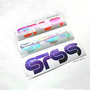 May include: Three stickers with the letters "srss" in different colors. The top sticker is hot pink opal, the middle is silver rainbow chrome, and the bottom is purple glitter. The stickers are on a white background.