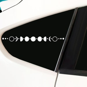 May include: A white car window with a black moon phase decal. The decal features a series of circles and crescents representing the different phases of the moon.