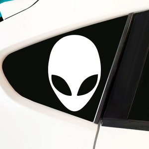 May include: A white alien head silhouette sticker on a black background. The sticker is applied to the back window of a white car.