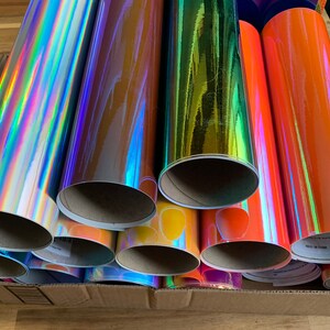 Peut inclure: Un ensemble de rouleaux de vinyle iridescent de diff&eacute;rentes couleurs, notamment argent, or, orange et bleu. Les rouleaux sont empil&eacute;s dans une bo&icirc;te en carton.