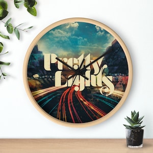 Puede incluir: Un reloj de pared redondo de madera con una imagen colorida de una autopista de noche con las palabras "Pretty Lights" en una fuente retro.