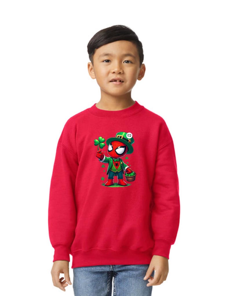 Puede incluir: Una sudadera roja con una imagen de dibujos animados de Spider-Man vestido de duende sosteniendo un tr&eacute;bol de cuatro hojas y una olla de oro. El texto "Happy St. Patrick's Day" est&aacute; impreso en la sudadera.