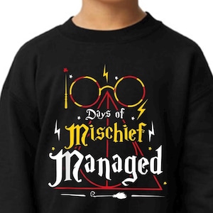 May include: Black sweatshirt featuring a graphic with the text "Days of Mischief Managed." The design includes yellow and red glasses, a wand, and a lightning bolt. The sweatshirt is a children's apparel item.